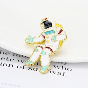Macro detail of cartoon astronaut enamel pin with gold plating and white paint finish