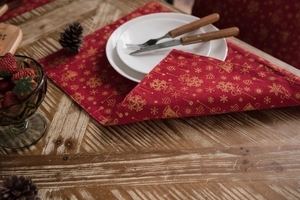 Close-up of red Christmas table runner with golden snowflakes and bells on wooden table