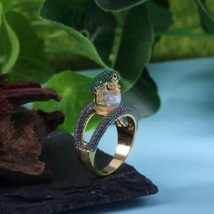 Artistic gold frog ring with green pave stones holding a pearl on black stone