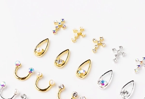 Makroaufnahme von Nagel-Anhängern in Gold und Silber mit Perlen, Strass und Kreuz-Motiven