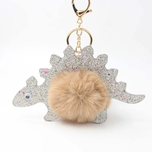 Cute cartoon dinosaur keychain with silver glitter finish and beige faux fur pompom