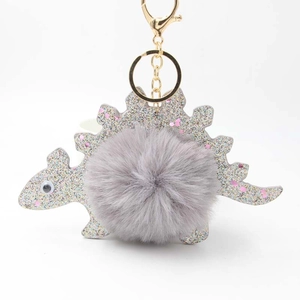 Detail of cute silver dinosaur keychain with grey plush ball and golden metal clasp