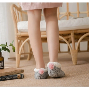Detail of warm grey fuzzy slipper socks with white plush trim and pink pom-poms on heel