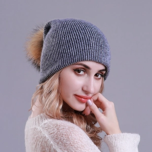 Detail of dark grey knit beanie with rib pattern and large raccoon fur pom-pom on model