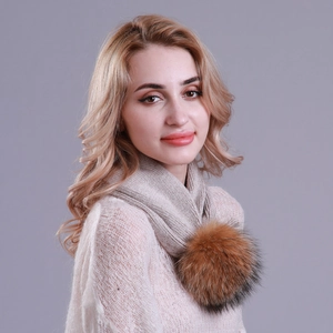 Detail of light beige knitted winter scarf featuring a fluffy brown faux fur pom pom accent