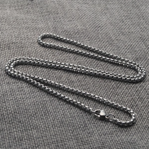 Macro shot of silver stainless steel box chain necklace with lobster clasp on grey linen