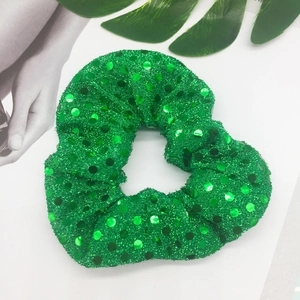 Green sequined hair scrunchie with emerald mesh on a stylish magazine background