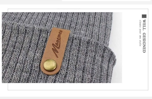 Detail of grey ribbed knit beanie with a brown leather logo tag and gold metal button
