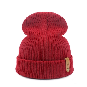 Detailed view of dark red rib-knit beanie with a brown leather label and metal button