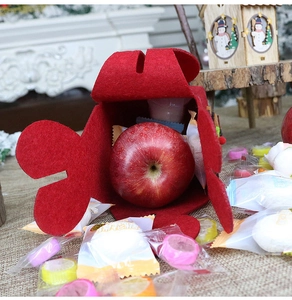 Detail of red felt Christmas gift bag with petal cutout design holding an apple
