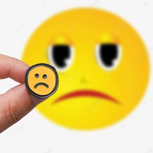 Gros plan d'un petit pin's en émail jaune avec un visage triste tenu par la main