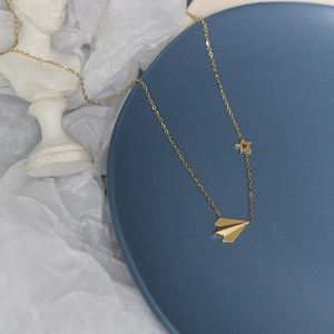 Detailed shot of gold paper plane and star necklace on artistic blue dish display