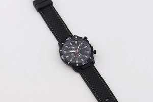 Detail of black sports watch dial with green indices and perforated silicone strap