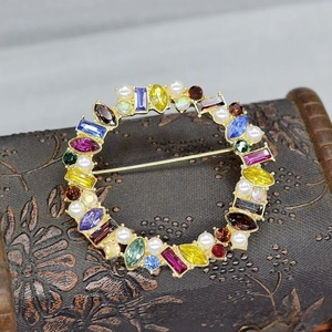 Macro detail of vintage matte gold brooch featuring colorful gemstones and pearls