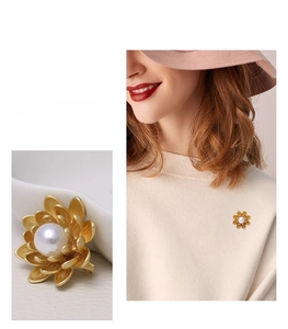 Detail of matte gold flower brooch featuring a central pearl and model styling