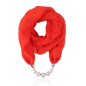 Detail of red chiffon scarf with pearl pendant and metal buckle on white background