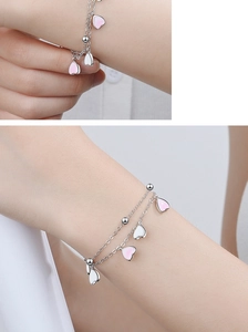 Detail of cherry blossom pink heart charms on a layered silver beaded bracelet