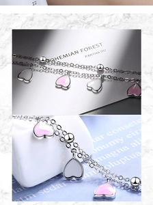 Detail of silver layered chain bracelet with pink and white heart charms on marble background