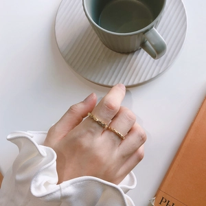Close-up of a gold rope-textured silver ring worn on a finger over a cozy lifestyle background