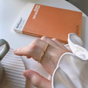 Detailed view of a gold twisted rope ring worn on finger with a stylish urban background
