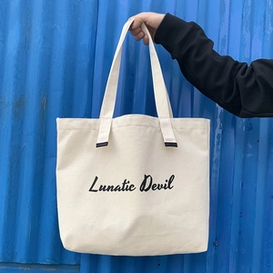 Detail of off-white canvas tote bag featuring black Lunatic Devil artistic font print