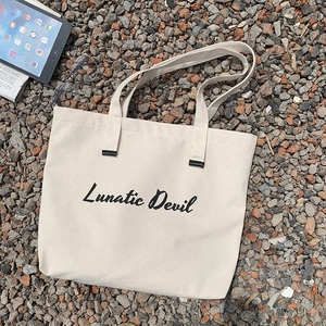 Detail of beige canvas tote bag with Lunatic Devil script logo on stone ground
