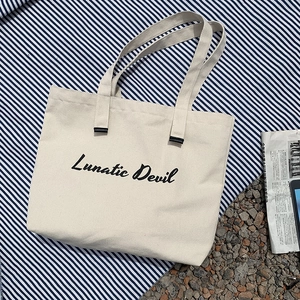 Close-up of Lunatic Devil printed off-white canvas tote bag on blue striped fabric