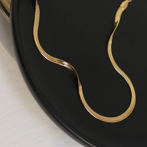 Detailed close-up of golden flat snake bone chain necklace on a matte black tray