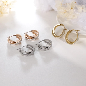 Intertwined gold and silver hoop earrings with diamond accents on a white floral base
