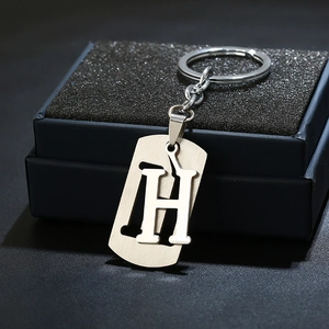 Detailed macro view of silver stainless steel letter H keychain on a dark blue gift box