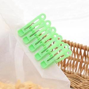 Set of 6 green plastic windproof clothes pegs securing bags on a woven basket
