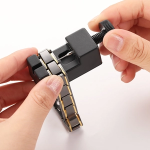 Close-up showing a link removal tool adjusting a black and gold magnetic therapy bracelet