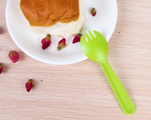Close-up of a green disposable spork on a wooden table next to a dessert plate