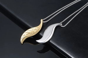 Detailed close-up of gold and silver leaf pendants on steel box chains over a dark surface