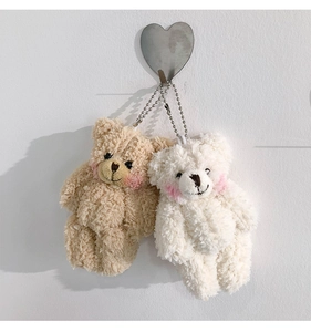 Close-up of beige and white plush bear keychains with metal bead chains on hooks