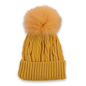 Detail of mustard yellow cable knit beanie featuring a large faux fur pom-pom on top