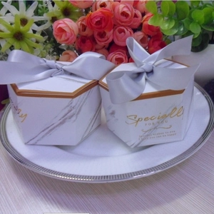 Macro shot of white marble gift boxes with gold foil text and silver ribbon bows