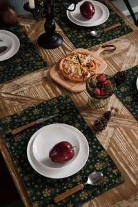 Close-up of green Christmas placemats with gold snowflakes on a wooden table set for a meal