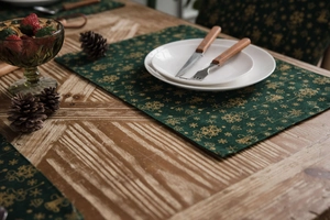Detail of green Christmas placemat with golden snowflakes on a rustic wooden table