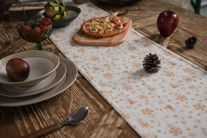 Flat lay of a white Christmas table runner with golden prints and holiday dinner decor