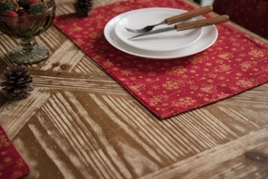 Close-up of red table runner with gold leaf patterns on a rustic wooden dining table