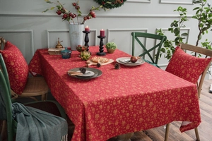 Close-up of red Christmas tablecloth and pillows with gold snowflake prints in warm setting