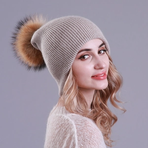 Detail of beige ribbed knit beanie with a fluffy raccoon fur pom-pom shown on model