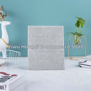 Vertical grey velvet earring display board showing holes for jewelry storage on desk