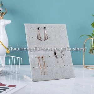 L-shaped gray velvet earring display stand with multiple holes on a marble surface