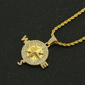 Close-up of golden compass pendant with sparkling rhinestones on a black textured surface