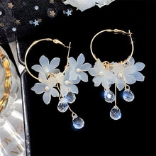 Detailed close-up of golden floral hoop earrings with white petals and crystal drops