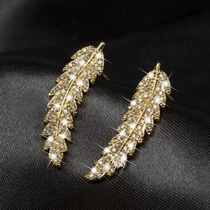 Close-up of golden feather earrings with shimmering pavé zircon on black silk background