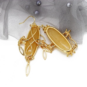 Detail of gold leaf earring with light yellow oval stone and textured mesh background