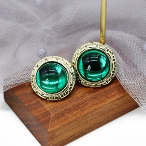 Macro shot of gold-plated geometric earrings with emerald green round gemstones